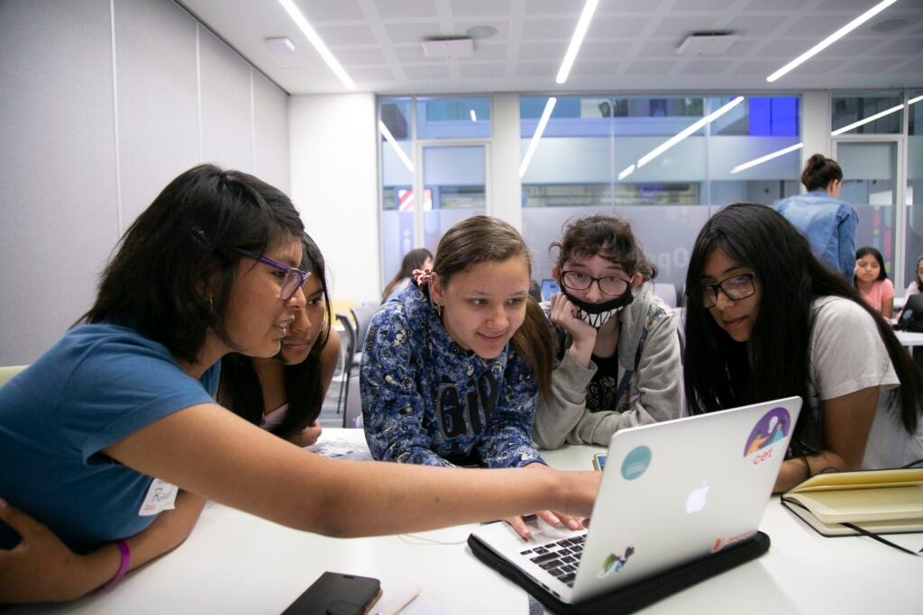 5 adolescentes mujeres miran una computadora como parte de las actividades de chicas en tecnología