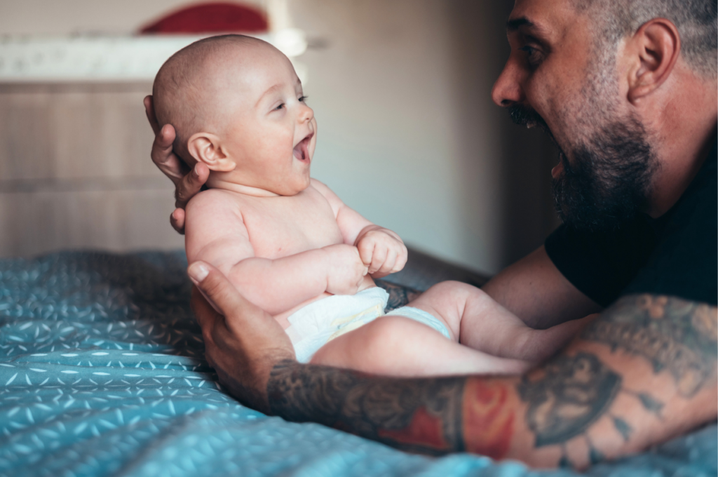 Padre joven con tatuajes sostiene a bebé sonriente