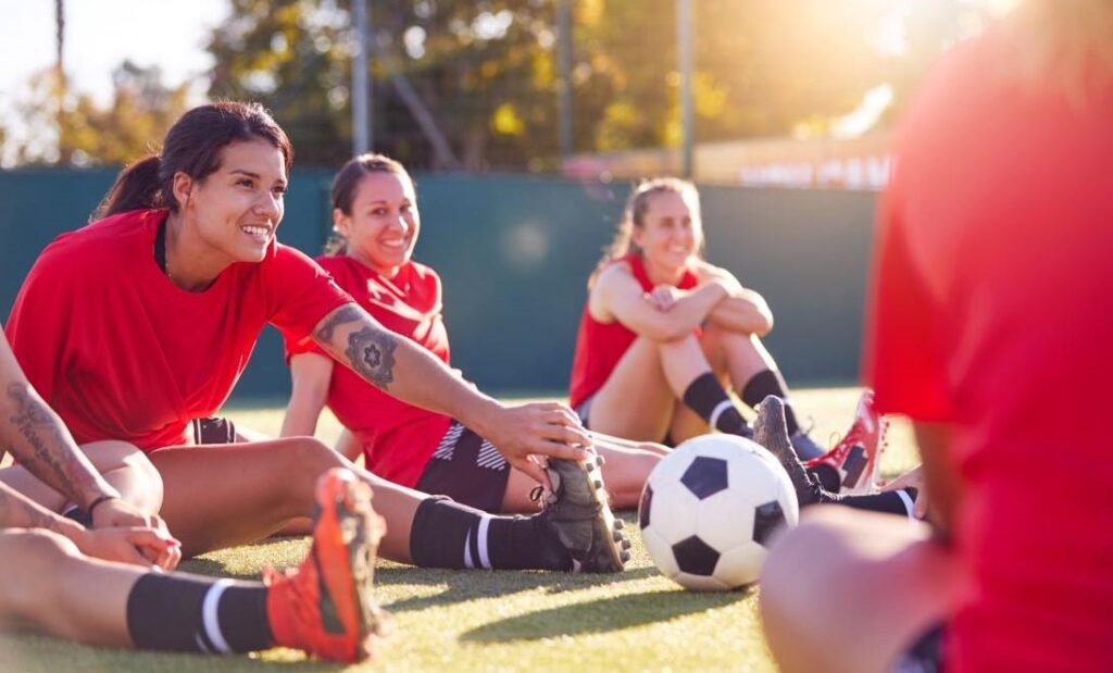 Futbolistas sonríen mientras hacen estiramientos en la cancha