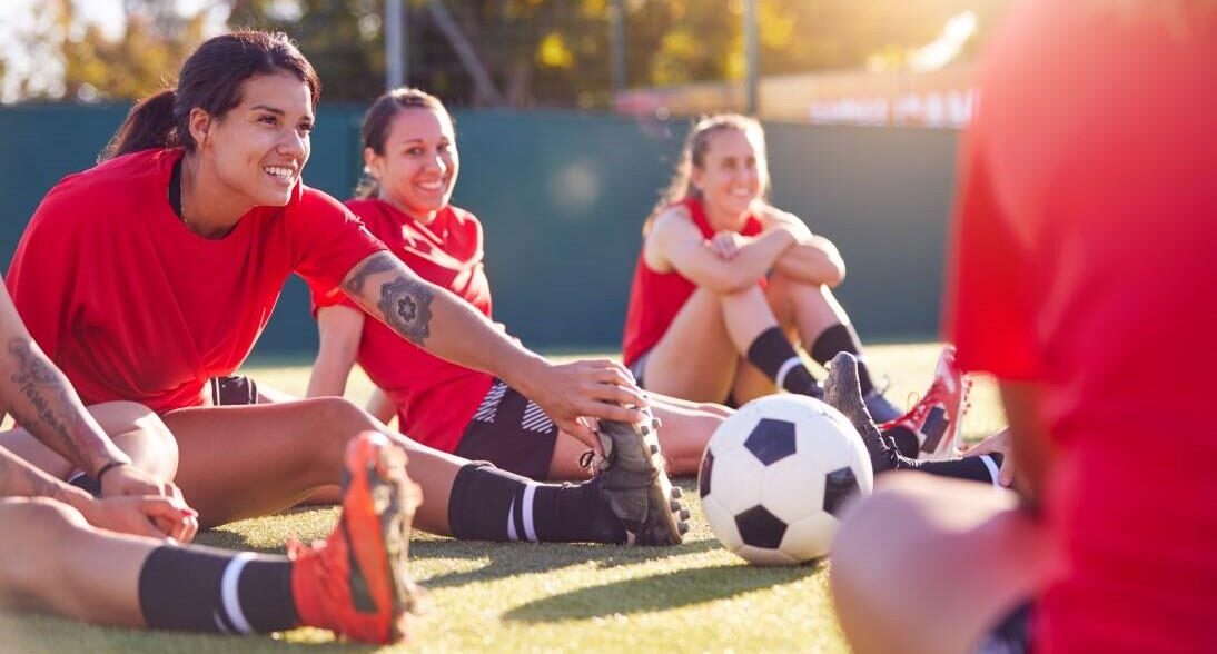 Futbolistas sonríen mientras hacen estiramientos en la cancha