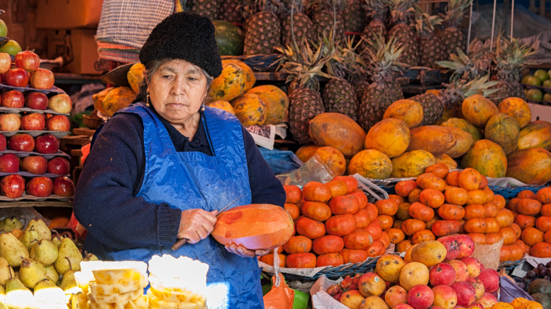 Una trabajadora adulta mayor atiende su puesto de frutas en un mercado